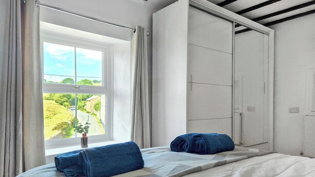 Un dormitorio con un ventanal grande, una cama con cubrecama estampado y una toalla azul sobre la cama.