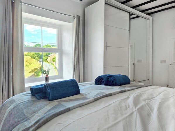 Un dormitorio con un ventanal grande, una cama con cubrecama estampado y una toalla azul sobre la cama.