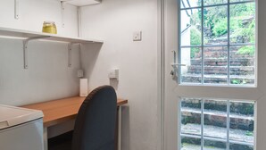 Habitación compacta con escritorio, silla y ventana con vistas a una escalera de ladrillo y vegetación.