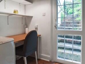 Habitación compacta con escritorio, silla y ventana con vistas a una escalera de ladrillo y vegetación.