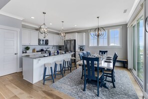 A modern kitchen with white cabinetry, stainless steel appliances, and a central island with bar stools. - Newly Listed Oceanfront Home, Large Heated Swim Spa, Elevator, Easy Beach Access (Oak Island)