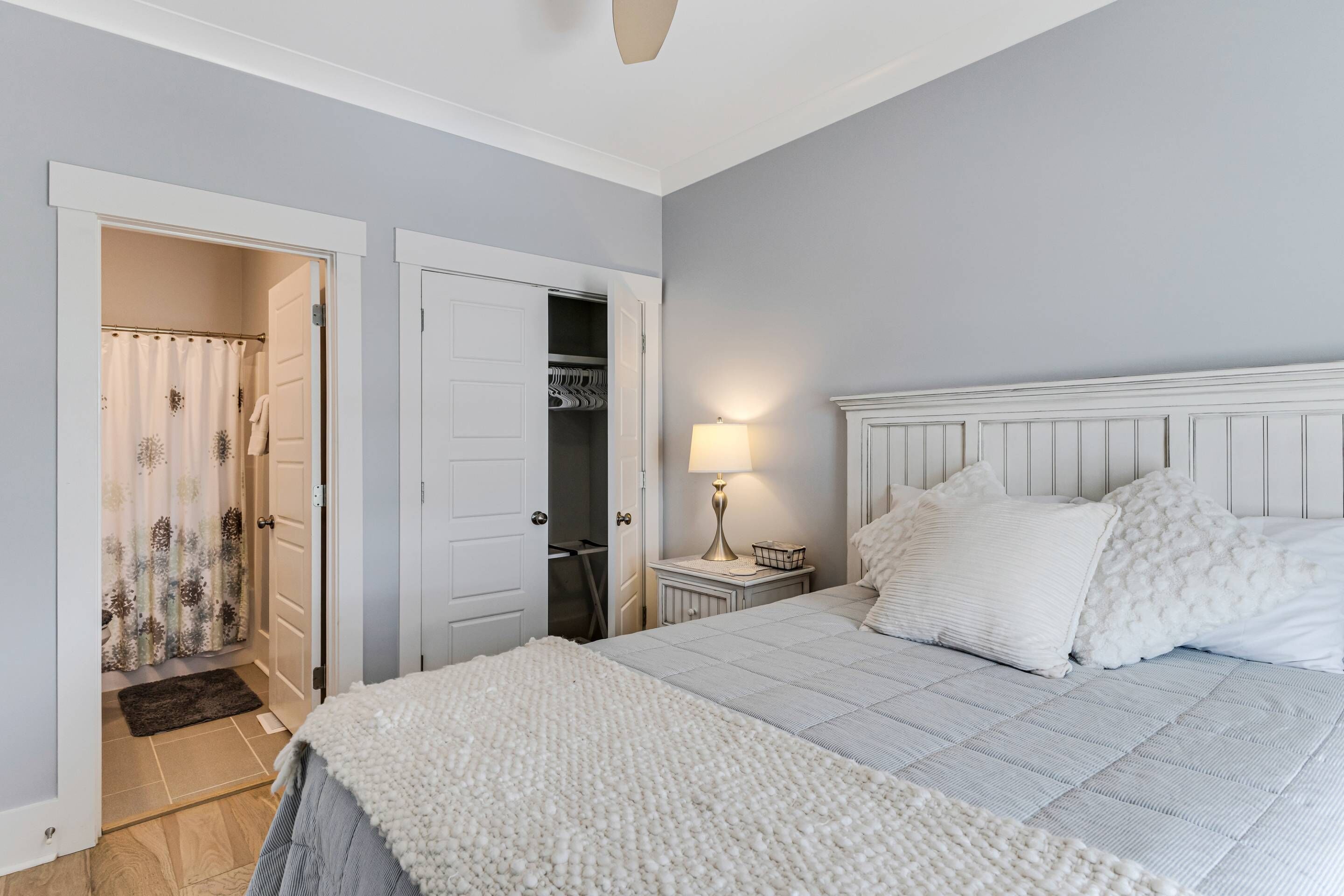 A bedroom with a bed, a nightstand, a lamp, a closet, and a shower area.