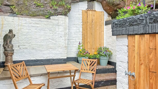 A small outdoor seating area with a wooden table and chairs, a statue, and potted plants.