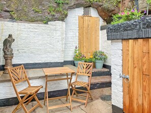 A small outdoor seating area with a wooden table and chairs, a statue, and potted plants. - 2 bedroom accommodation in Leek (Leek)