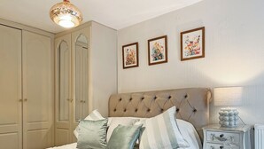 A neatly arranged bedroom with a large bed, a bedside table with a lamp, and three framed floral paintings on the wall.