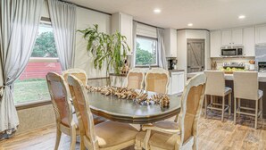 Un coin repas avec une table ronde entourée de six chaises, une cuisine avec des meubles blancs, un four à micro-ondes et un réfrigérateur.
