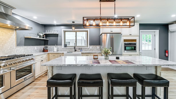 Cozinha moderna com uma ilha grande, eletrodomésticos de aço inoxidável e banquetas pretas.