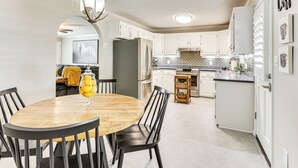A modern kitchen with white cabinets, a stainless steel refrigerator, and a wooden dining table with chairs.