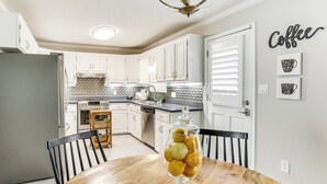 A kitchen with white cabinets, a wooden dining table, and a fruit bowl.