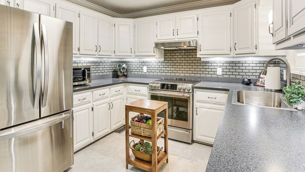 A modern kitchen with white cabinets, stainless steel appliances, a brick backsplash, and a wooden island with baskets.