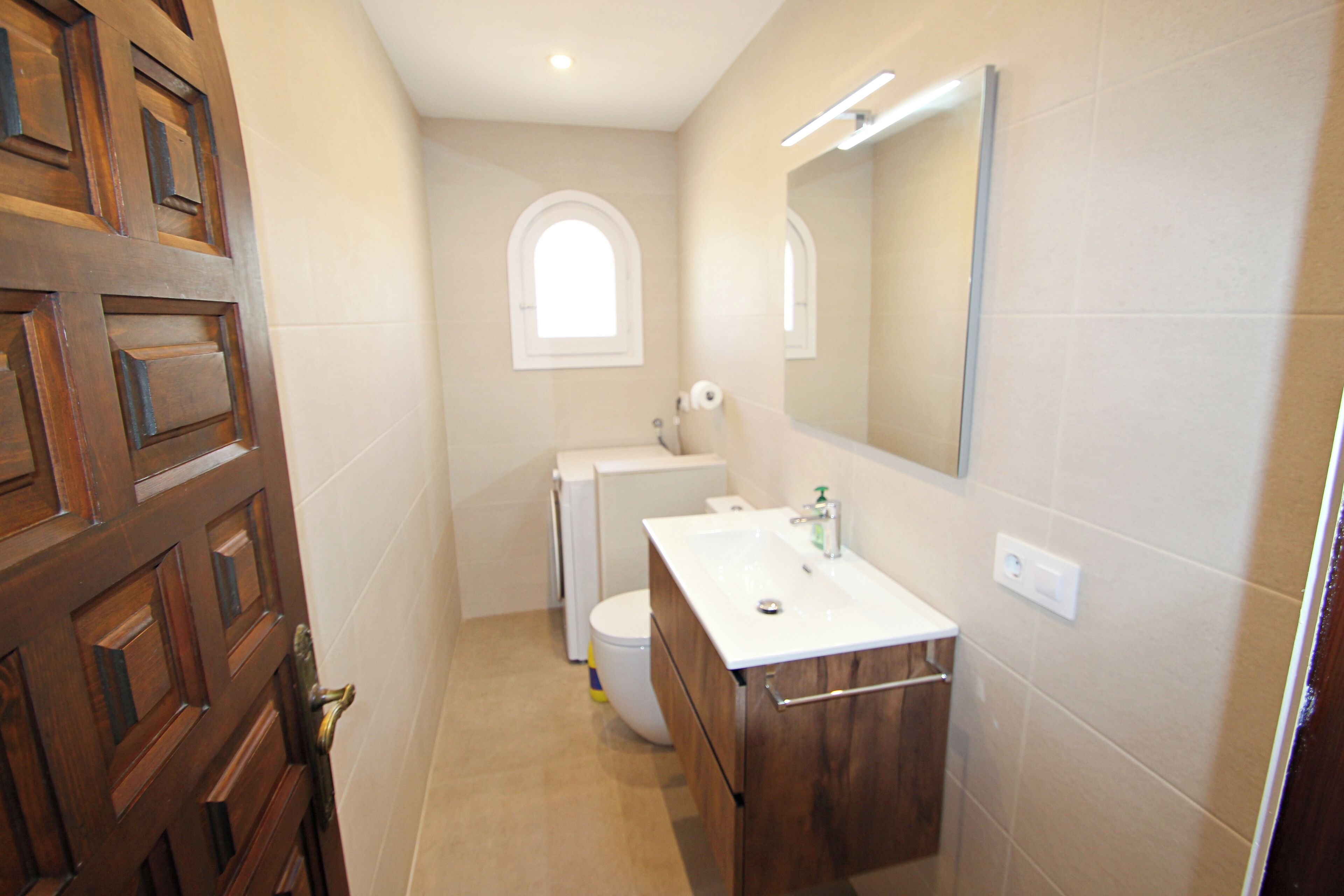 A bathroom with a wooden door, a white sink, a toilet, and a mirror.