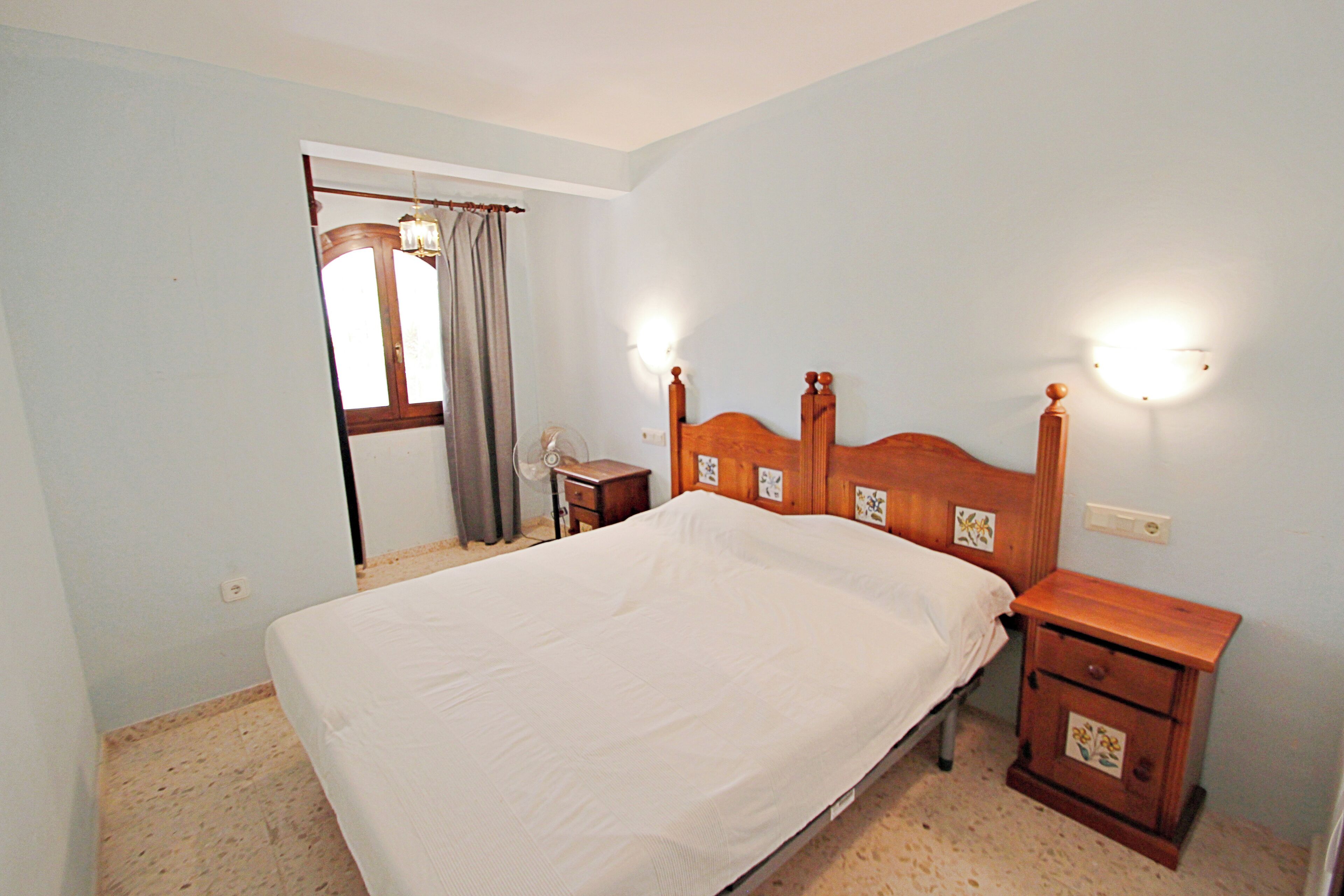 A bedroom with a wooden bed, bedside tables, a nightstand, a mirror, and a window with curtains.