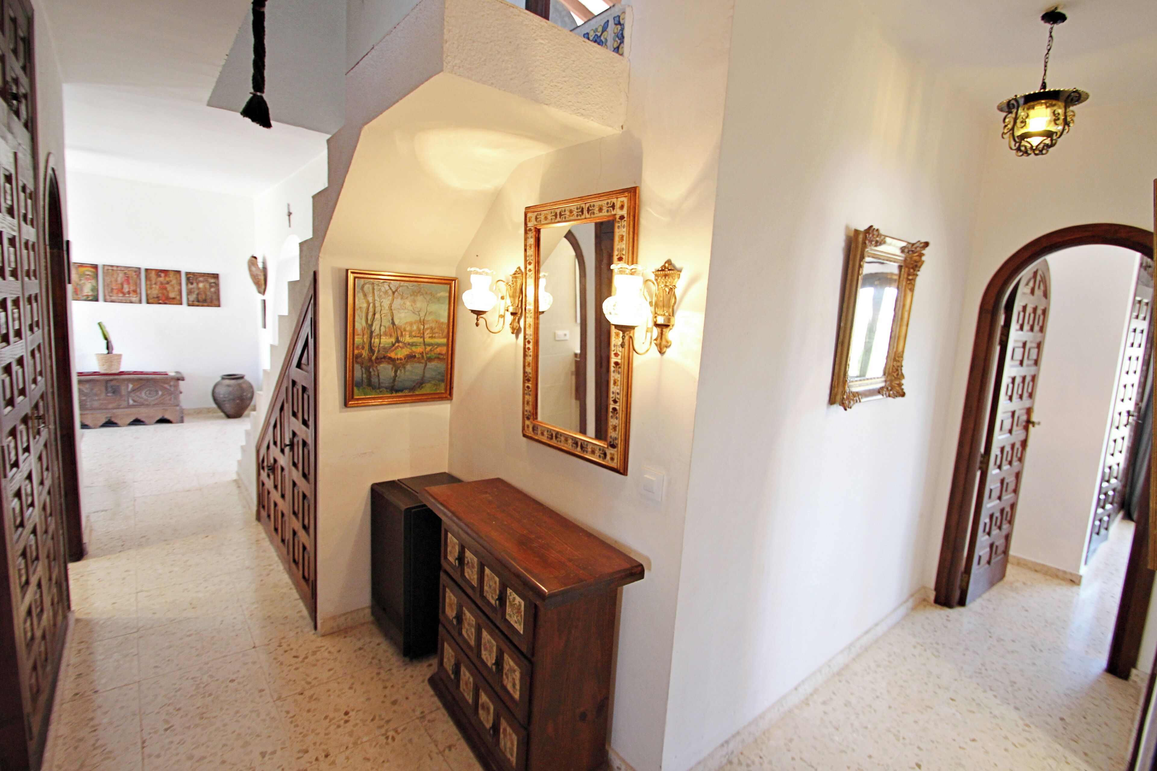 Un pasillo con un banco de madera, un espejo grande y apliques de pared.