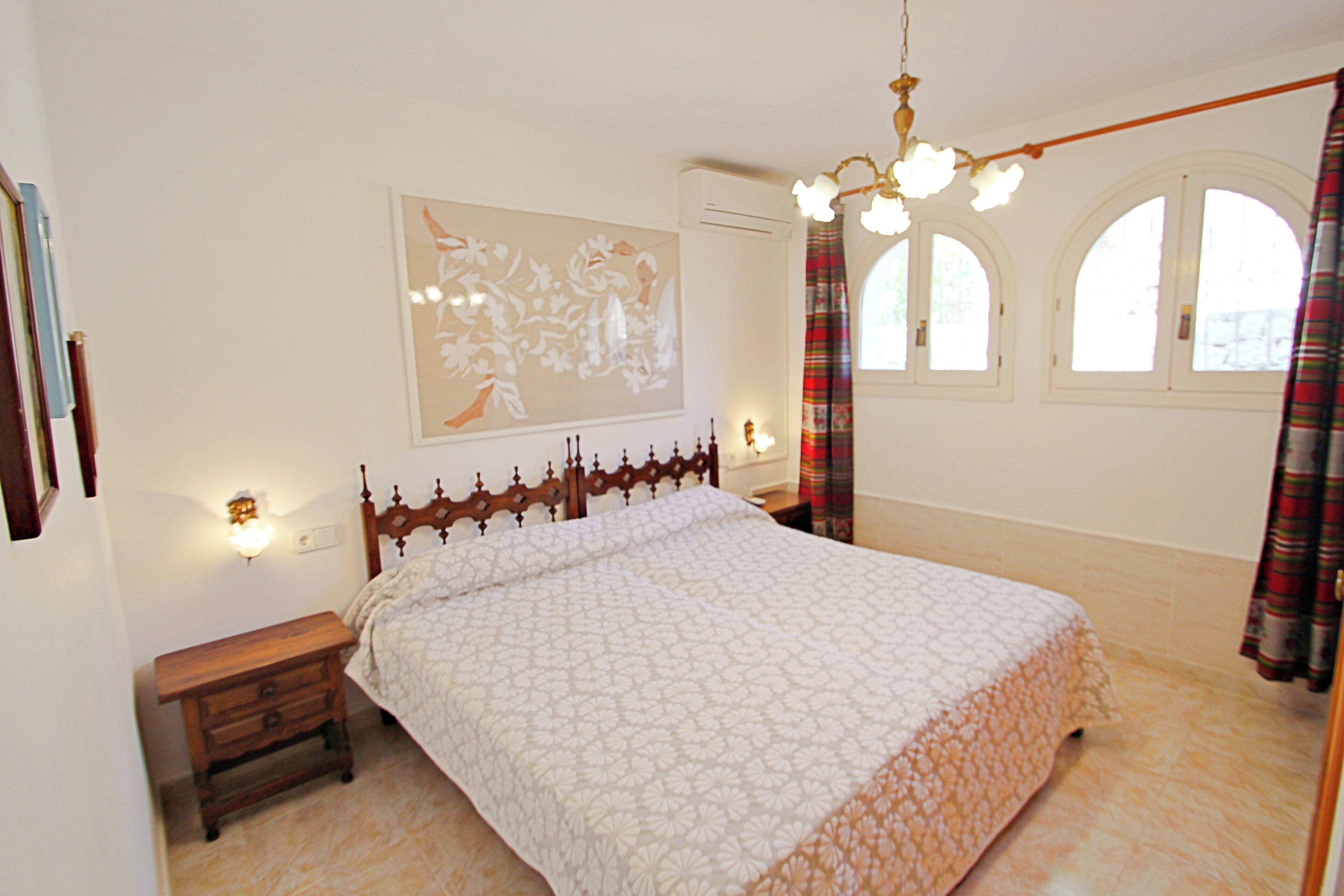 A bedroom with a large bed, a nightstand, a wall-mounted light, and a window with curtains.