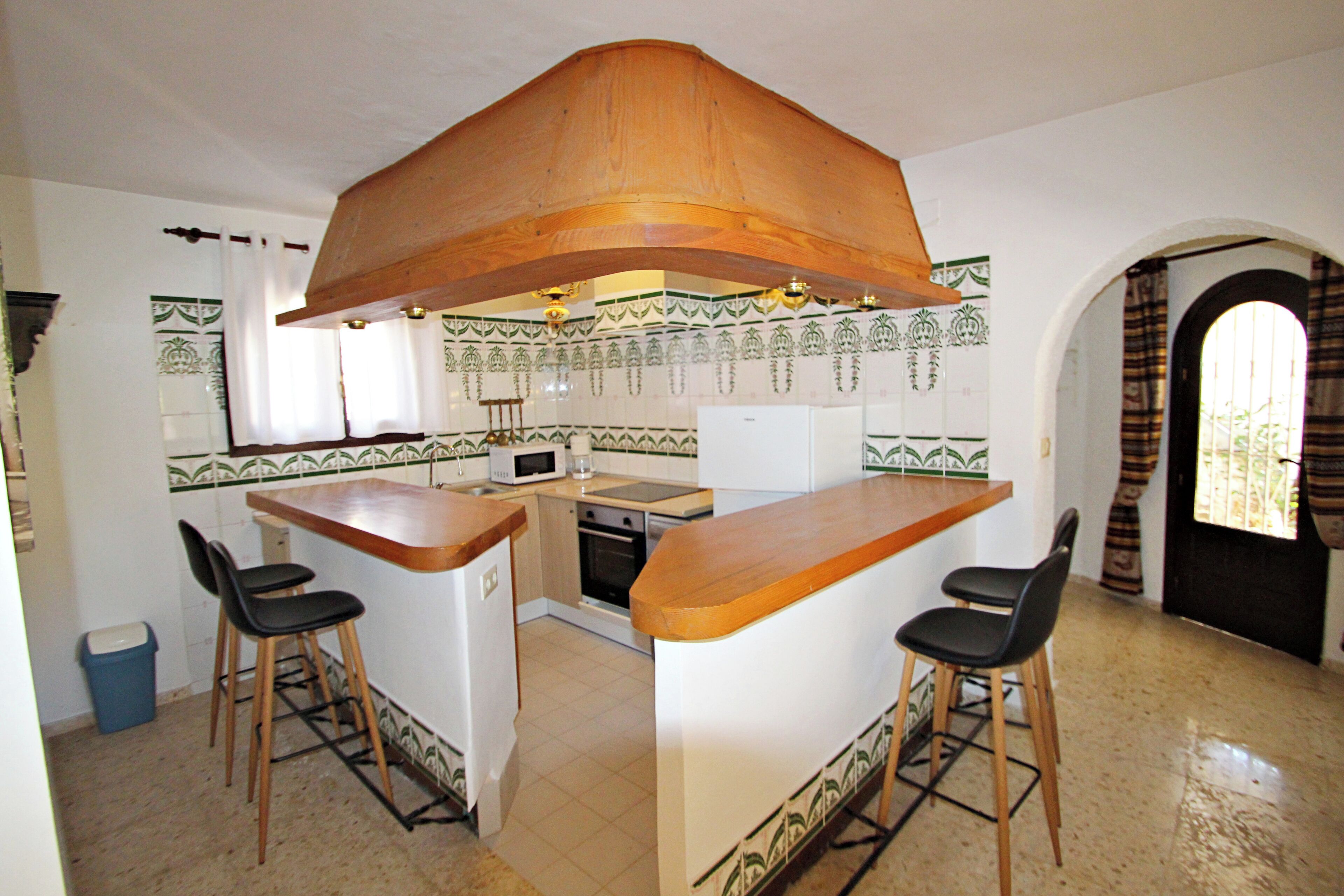 Une cuisine avec un îlot central en bois, deux tabourets de bar, un four à micro-ondes et un évier.