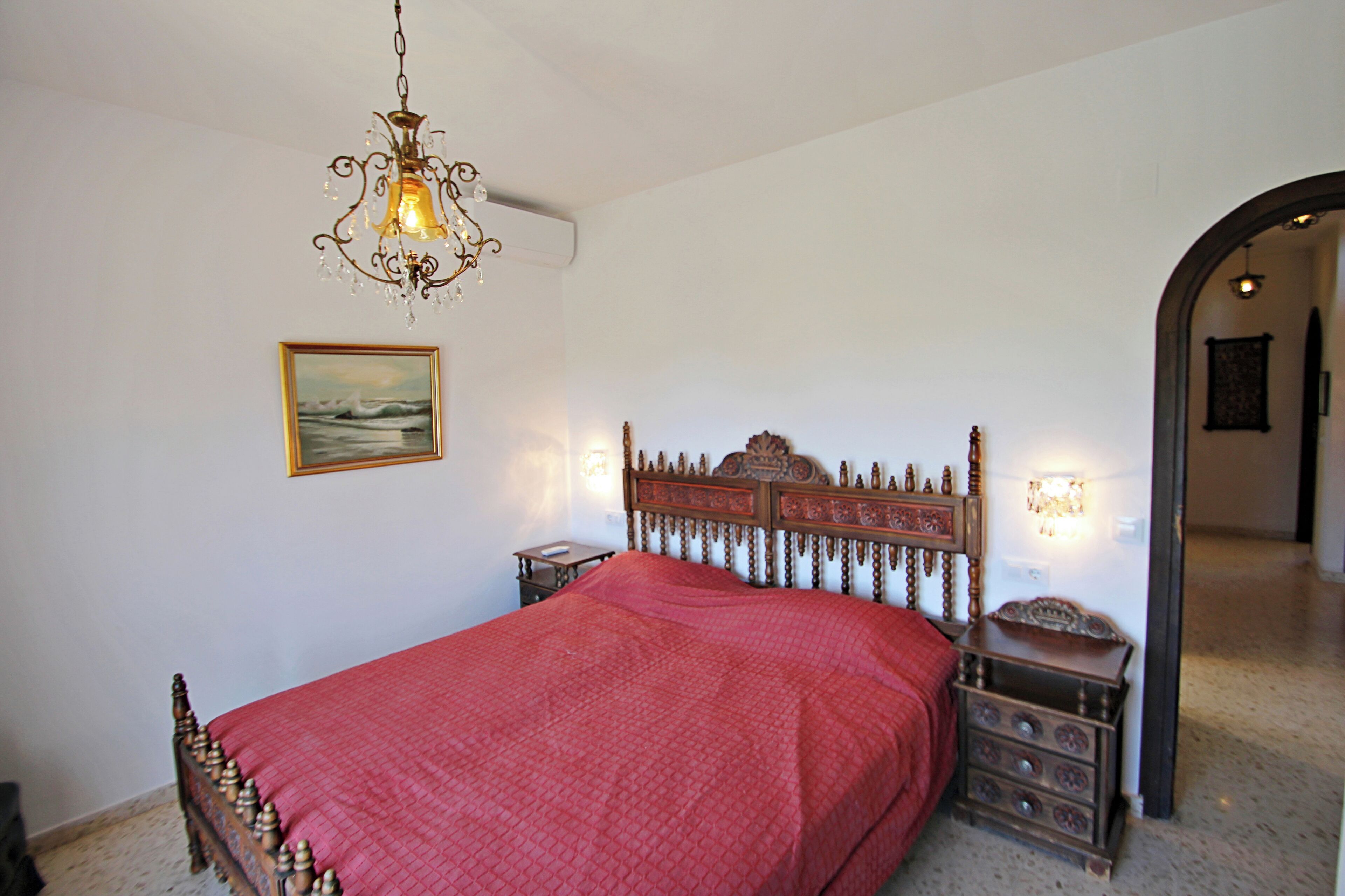 Una camera da letto con un letto in legno, un lampadario, un comodino e una lampada a parete.