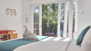 A bedroom with a bed, a desk, and a chair. There is a window with a view of greenery outside. - The shortcut rooms (Canggu)