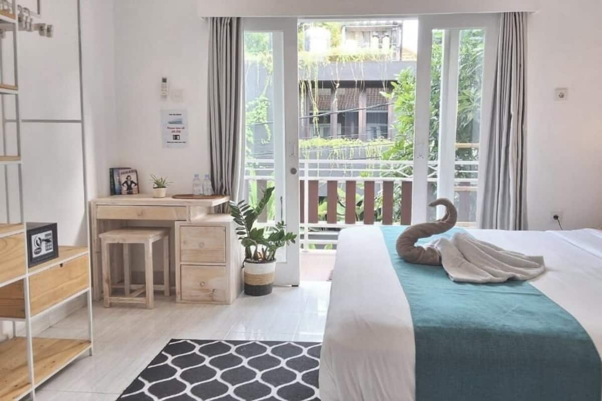 A bedroom with a bed, a desk, a chair, a potted plant, and a view of the outside.