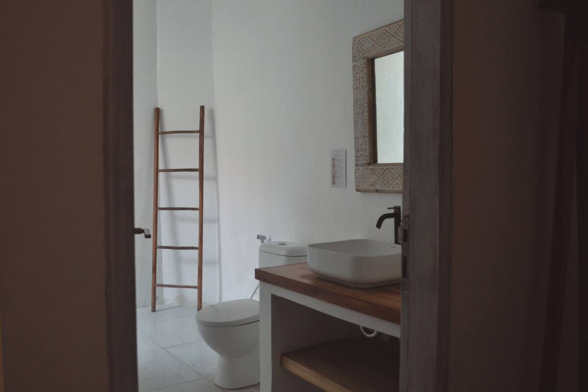 A bathroom with a toilet, a wooden ladder, and a sink with a mirror above it.