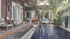 A pool area with a tiled deck, lounge chairs, and potted plants. - The shortcut rooms (Canggu)