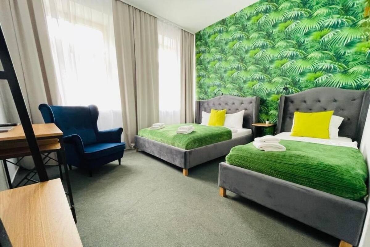 Ein Hotelzimmer mit zwei Betten, einem Schreibtisch, einem Stuhl und einer Wand mit grünem Blattmuster.