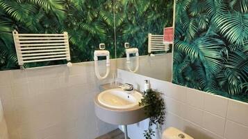 A bathroom with a white sink, toilet, and a mirror above the sink. The walls are covered with a green leafy wallpaper.