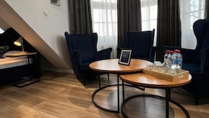 Een moderne kamer met twee donkerblauwe fauteuils, een houten salontafel met een dienblad met glazen en flessen, en een bureau met een lamp.
