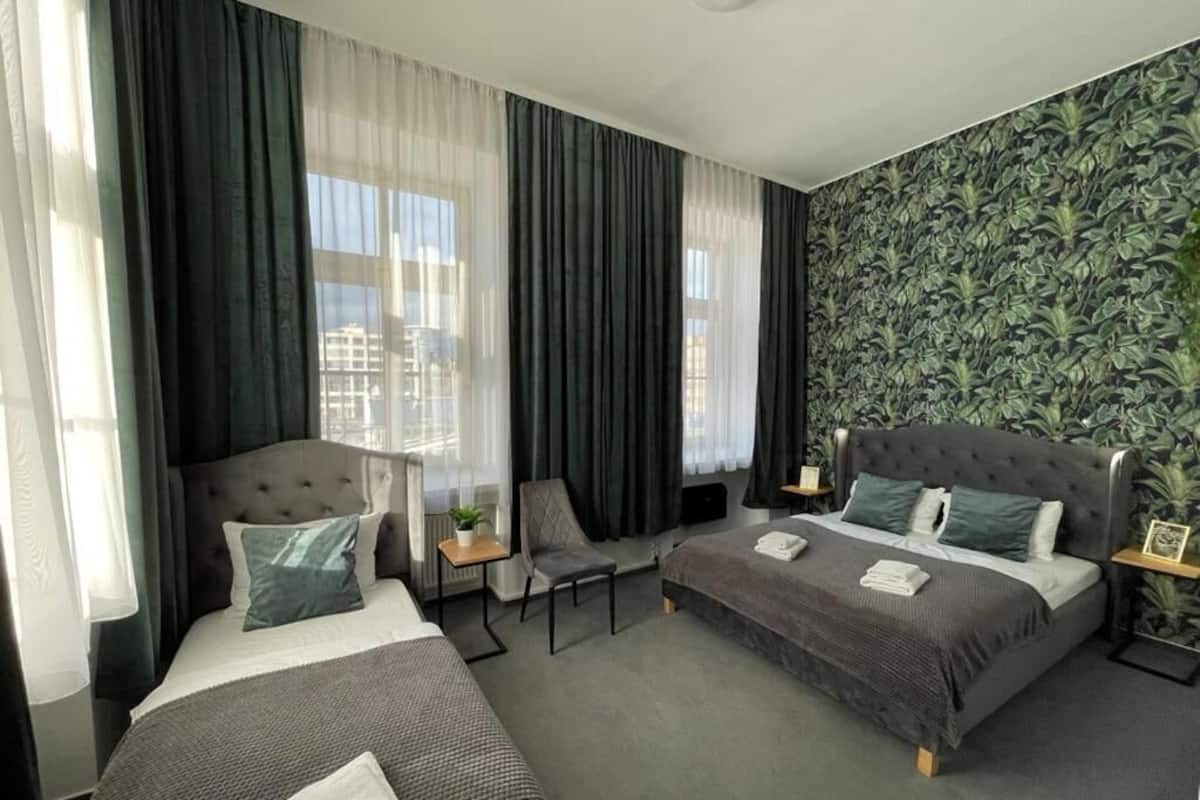 Ein modernes Hotelzimmer mit zwei Betten, einem Sessel, einem kleinen Tisch und Blick auf die Stadt durch große Fenster.