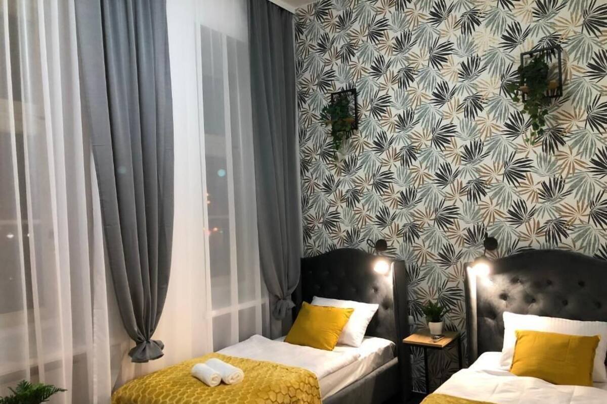 Ein Hotelzimmer mit zwei Betten, jeweils mit Kopfteil, einem kleinen Nachttisch und einer Zimmerpflanze.