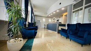 Een hotel lobby met een receptiebalie, blauwe banken, een potplant en een betegelde vloer.