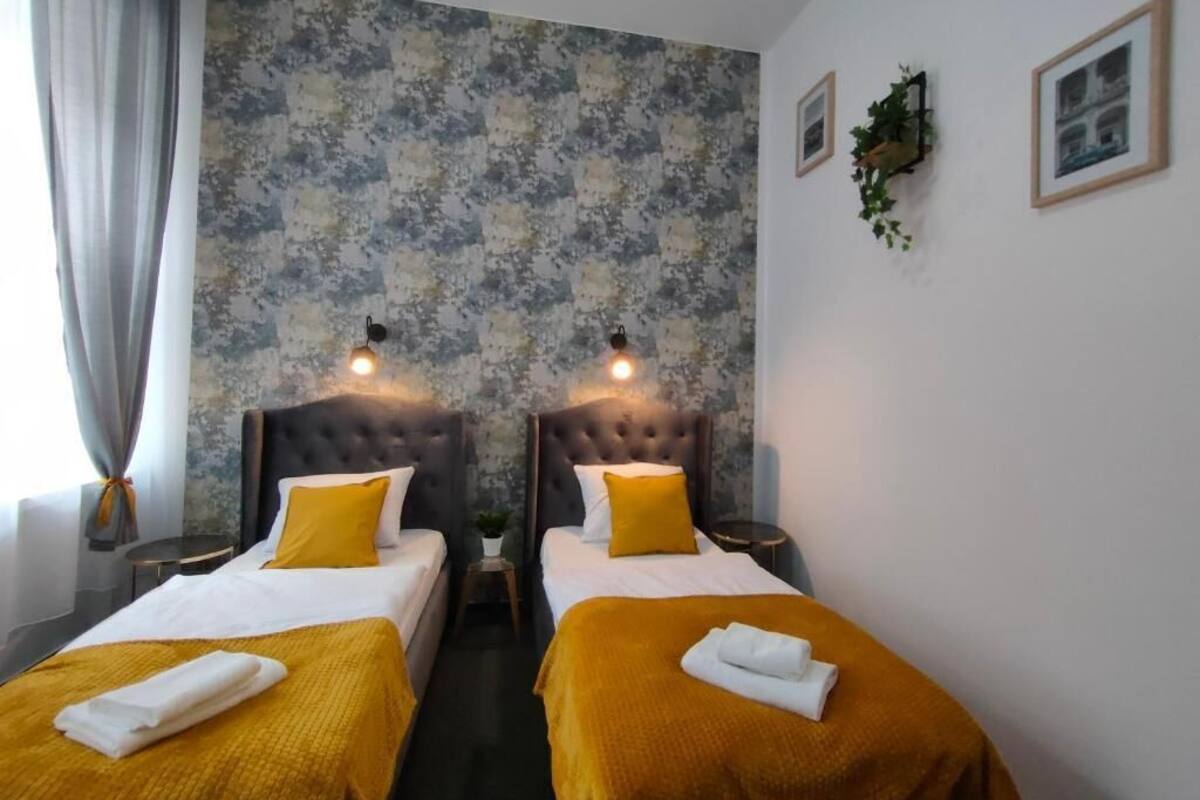 Ein Hotelzimmer mit zwei Betten, jeweils mit Kopfteil, einem großen Fenster mit Vorhängen und einer Wand mit einer strukturierten Oberfläche.