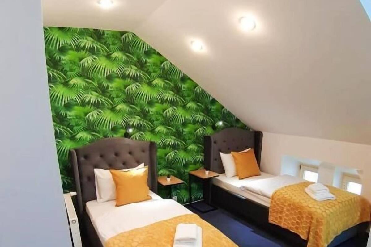Ein Hotelzimmer mit zwei Betten, jeweils mit Kopfteil, einer Wandmalerei von Grünpflanzen und einer Decke mit Einbautenbeleuchtung.