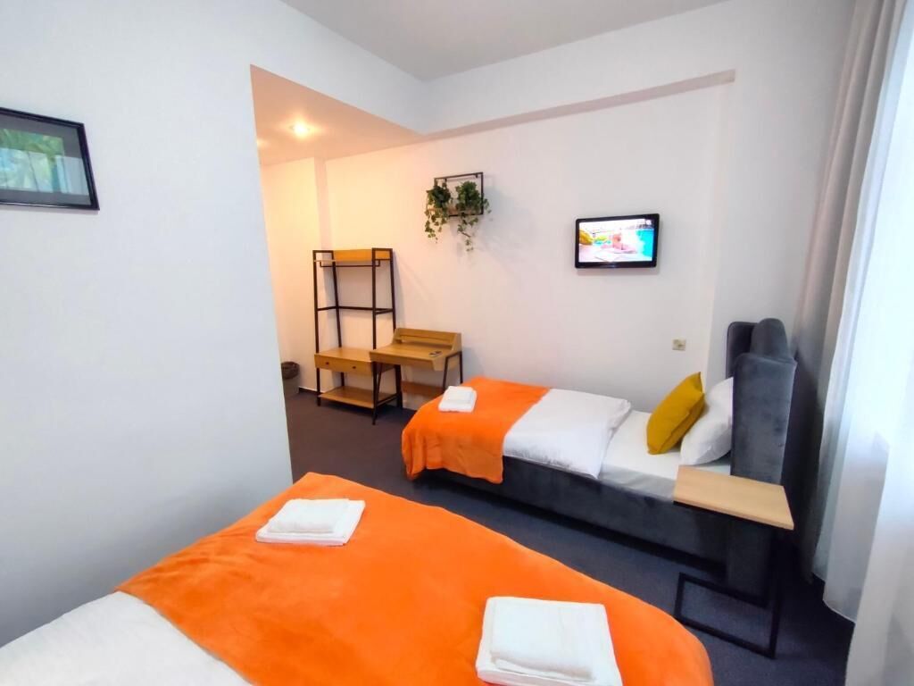 Ein Hotelzimmer mit zwei Betten, einem Schreibtisch, einem Sessel, einem Fernseher und einer Pflanze.