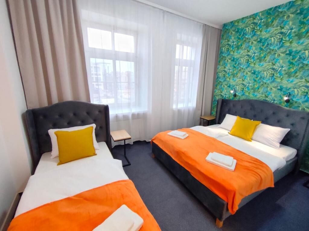 Et hotelværelse med to senge, hver med sengegavl, et vindue med let gardin og en væg med blomstermønster.