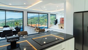 A modern kitchen with a large island, a dining area with a view, and a living space with a sofa and a TV. - GuestReady - Sunset Heaven Villa (Calheta)