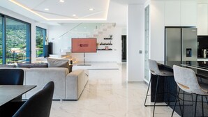 A modern hotel room with a large window, a sofa, a dining area, and a kitchen. - GuestReady - Sunset Heaven Villa (Calheta)