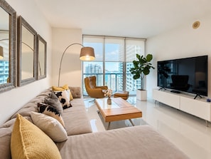 A modern living room with a sofa, armchair, coffee table, and a TV. - LUXURY 1BR/1BA ICON-BRICKELL MIAMI (Miami)