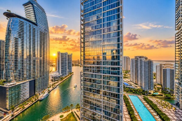 A high-rise building with a glass facade, a waterfront promenade, and a pool area.