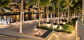 A nighttime view of a waterfront hotel with palm trees, a pool, and illuminated pathways. - LUXURY 1BR/1BA ICON-BRICKELL MIAMI (Miami)