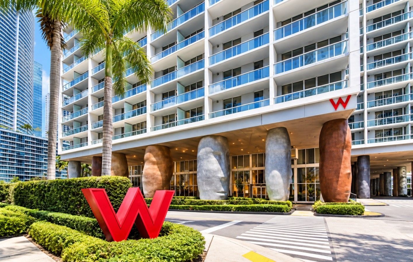 A modern hotel with a prominent 'W' logo, multiple floors, and a landscaped entrance with palm trees.