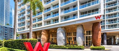 Hotel moderno com o logo 'W' em destaque, vários andares e entrada arborizada com palmeiras.