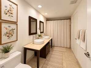 A bathroom with two sinks, a toilet, a shower curtain, and framed botanical prints on the wall.