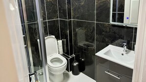 A modern bathroom with a glass shower enclosure, a white toilet, a sink with a mirror, and a cabinet with drawers. - Two bed flat cobh (Cobh)