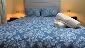 A neatly made bed with a blue patterned bedspread and two matching pillows, a folded white towel on the bed, and two bedside lamps on nightstands. - Two bed flat cobh (Cobh)