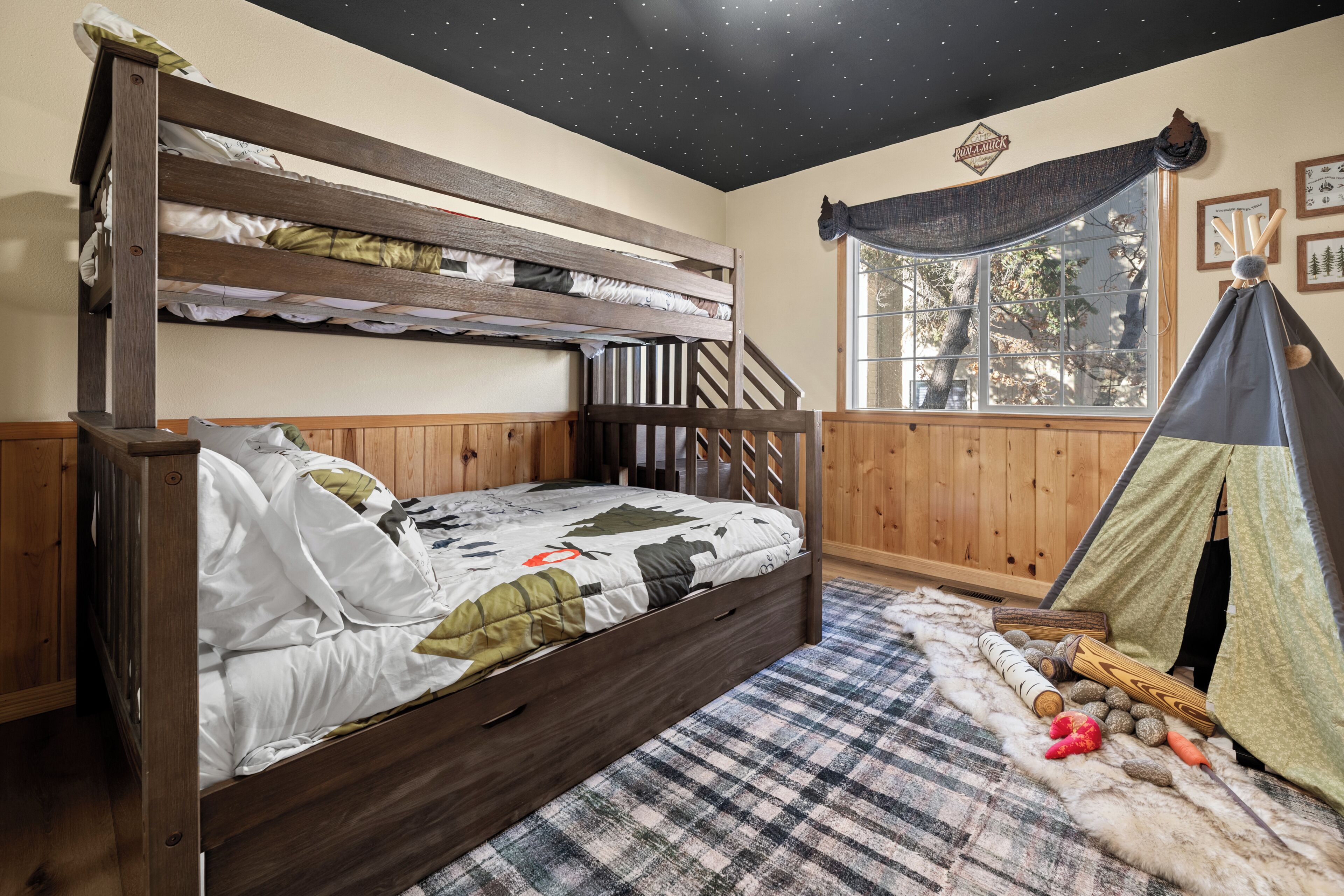 A bunk bed with a starry ceiling, a window with a view of trees, and a teepee-like tent structure.
