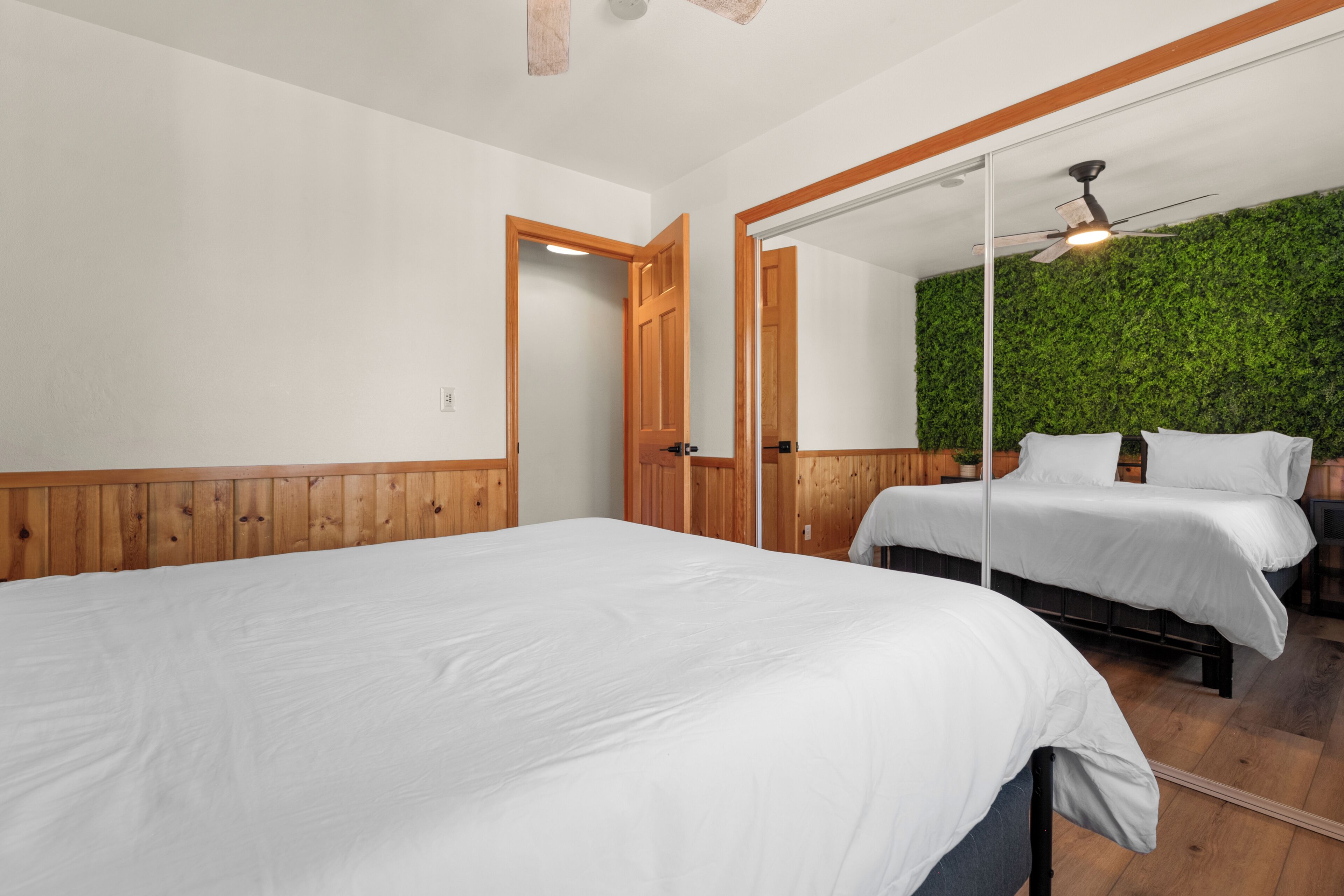 A bedroom with two beds, wooden paneling, a green wall, and a ceiling fan.