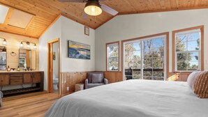 Une chambre avec un grand lit, un plafond en bois et une vue sur les arbres par les fenêtres.