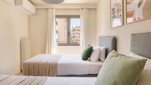 A hotel room with two beds, a radiator, a window with curtains, and a view of buildings outside.