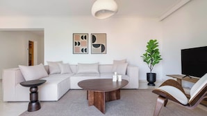 A modern living room with a sectional sofa, a round coffee table, a side table, a potted plant, and a flat-screen TV.