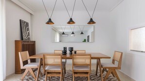 A dining area with a wooden table and chairs, pendant lights, a rug, and a mirror on the wall.